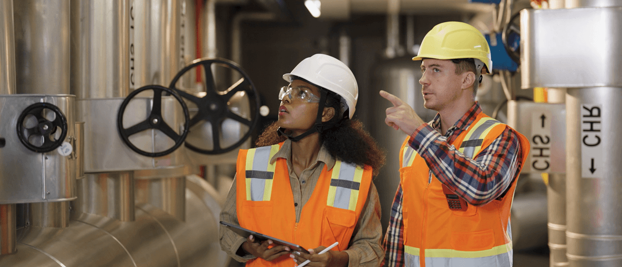 Engineers in orange safety vests at industrial pipe facility